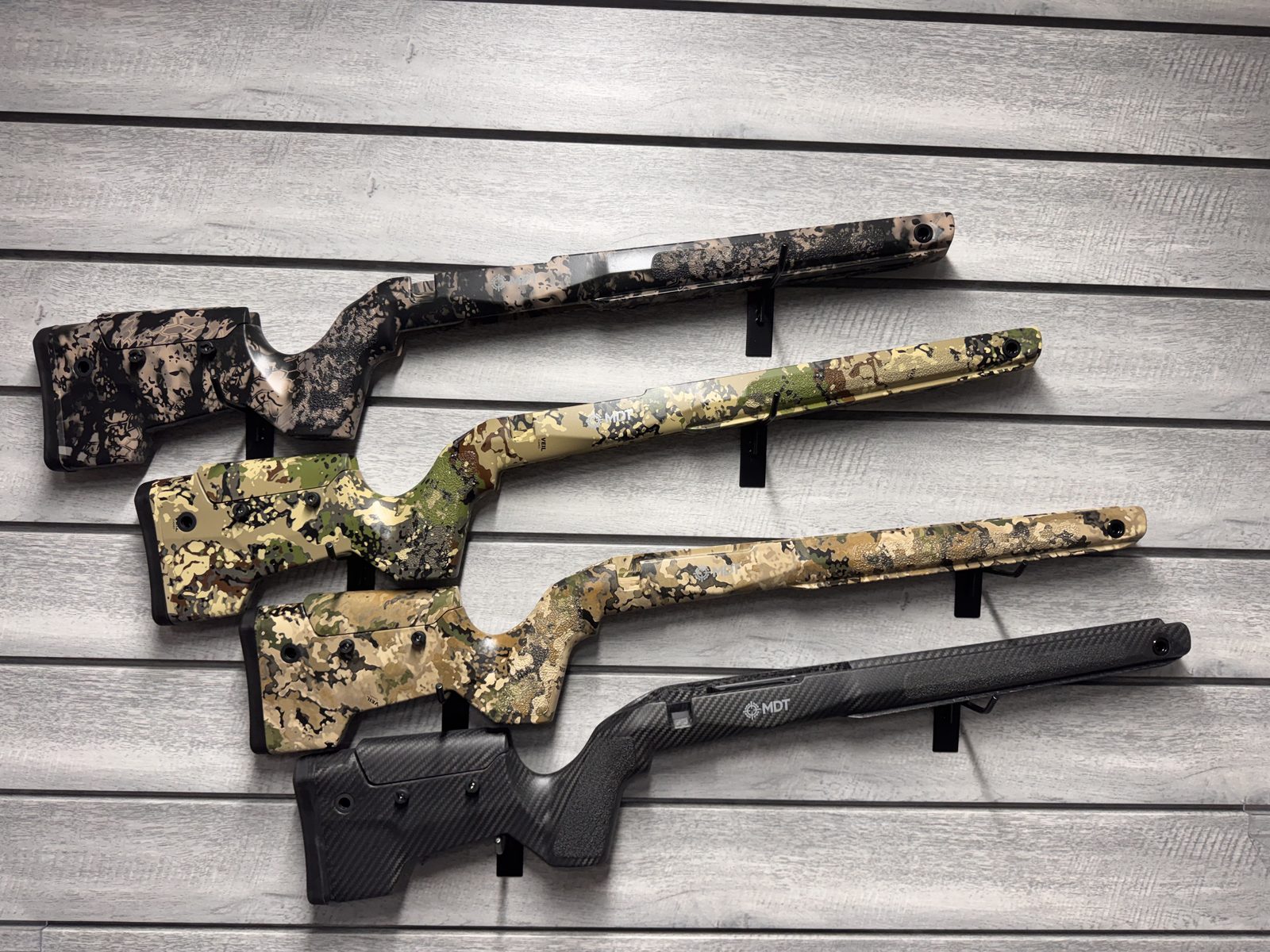 Four MDT hunting stocks on wall display — camo patterns and carbon fiber