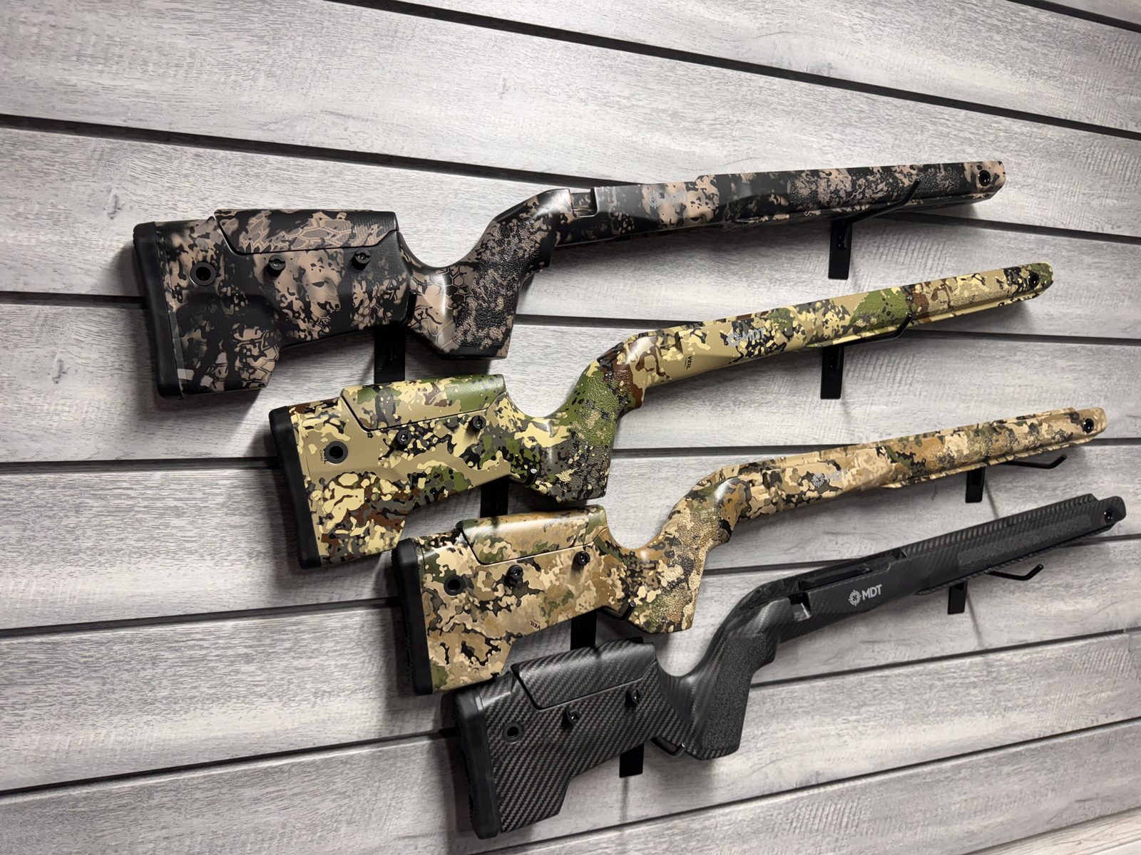 MDT stock lineup on wall display, angled view — Kryptek, Veil camo, and carbon fiber